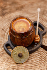 Open barrel with fragrant honey and honey stick in it on a textured wooden saw.