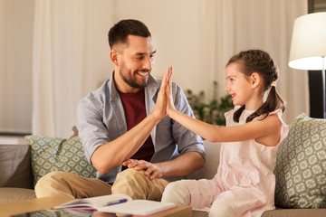 education, family and homework concept - happy father and daughter with book writing to notebook at home