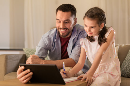 Education And Family Concept - Happy Father And Daughter With Book And Tablet Computer Doing Homework Together At Home