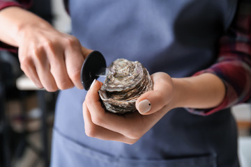 Woman opening raw oyster with knife, closeup