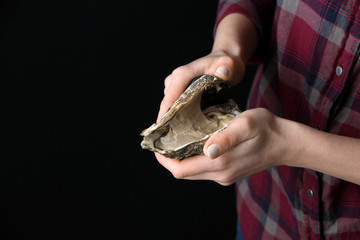 Woman opening raw oyster with knife against dark background, closeup