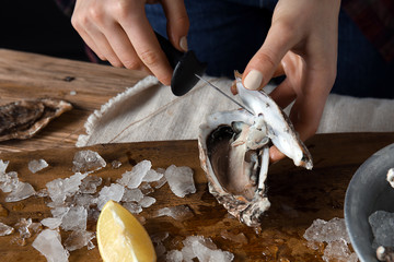 Woman opening raw oyster with knife at table, closeup
