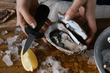 Woman opening raw oyster with knife at table, closeup