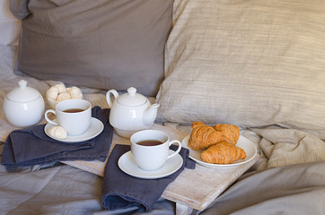 Romantic breakfast in bed for two. Teapot and two cups, croissants and meringue on the tray with flowers. Scandinavian style.