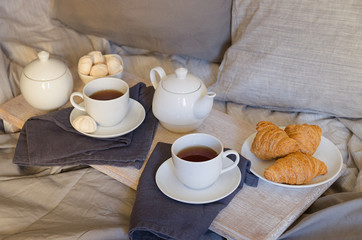 Romantic breakfast in bed for two. Teapot and two cups, croissants and meringue on the tray with flowers. Scandinavian style.