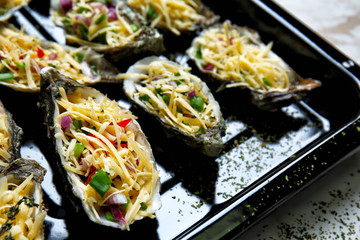 Tasty oysters with cheese and vegetables on baking sheet, closeup