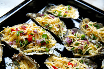 Tasty oysters with cheese and vegetables on baking sheet, closeup