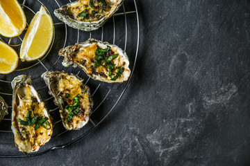 Cooling rack with tasty baked oysters and lemon on dark background