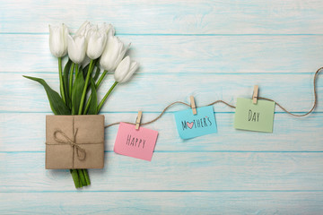 A bouquet of white tulips and envelope with a color stickers with clothespins on a rope and blue wooden boards . Mother's day