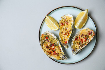 Plate with tasty baked oysters and lemon on grey background