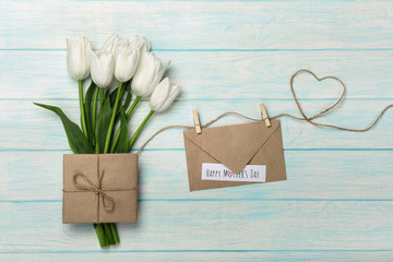 A bouquet of white tulips with a love note and envelope on a heart-shaped rope and blue wooden boards . Mother's day