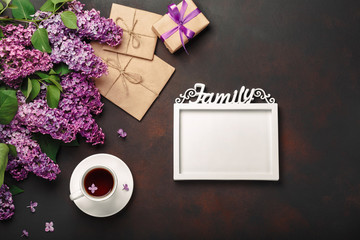 Obraz na płótnie Canvas A bouquet of lilacs with cup of tea, a white frame for inscription, gift box, craft envelope, a love note on rusty background
