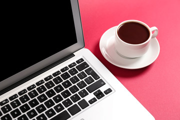 Fototapeta premium Modern laptop and cup of coffee on color background, closeup
