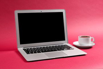 Fototapeta premium Modern laptop and cup of coffee on color background