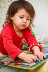 little girl Caucasian appearance in pajamas collects puzzles in a room