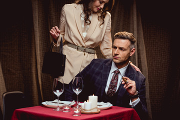 woman embracing man with cigar during romantic dinner in restaurant