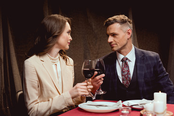 couple sitting at table and clinking glasses of red wine during romantic date in restaurant