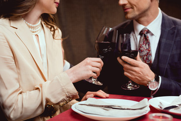 partial view of couple clinking glasses of red wine during romantic date in restaurant