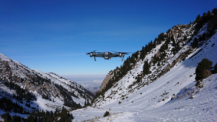 The quadcopter weighs in the air in the mountains. Mavic flies in the mountains. View of the gorge, blue sky and snowy mountains. A small drone in the mountains. Shooting a drone.