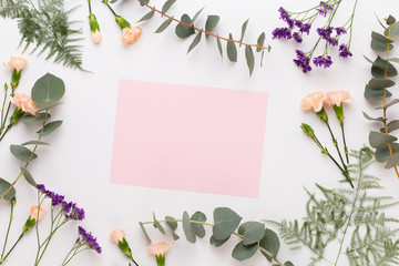 Flowers composition. Paper blank, carnation flowers, eucalyptus branches on pastel  background. Flat lay, top view, copy spaceFlat lay stiil life.