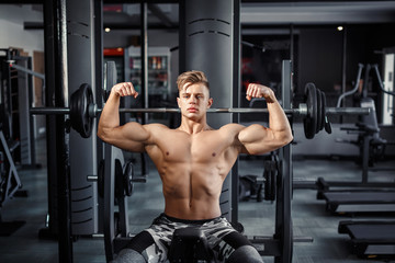 Fototapeta na wymiar Close Up of a muscular young man lifting weights in gym on dark background