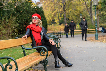 Fototapeta premium Blonde Dame mit rotem Schal auf Parkbank