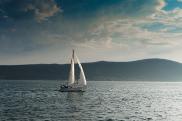 Fototapeta na wymiar Boat on the blue sea with clouds and mountains on the background