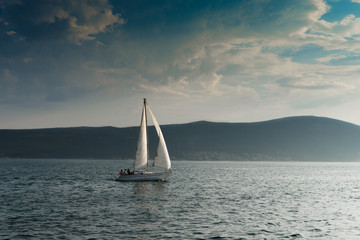 Fototapeta premium Boat on the blue sea with clouds and mountains on the background