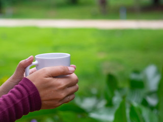 Close-up of hands holding a cup of coffee in the garden.