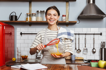 Happy young woman standing at the kitchen at home
