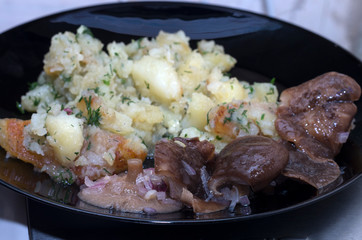 Potatoes with canned mushrooms on a glass plate in black.