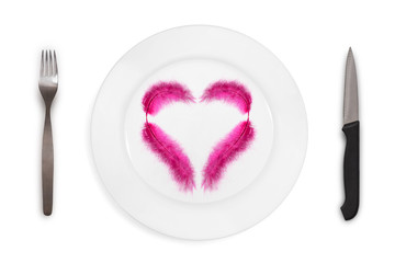 Top view on  a plate with pink feather in the heart shape on a white background. Concept of healthy and light food. Isolated