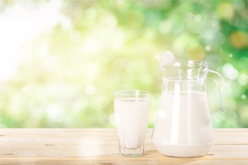 A glass of milk and a milk jug on plaid tablecloth