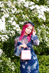 portrait of a beautiful girl with pink hair standing near flowers.