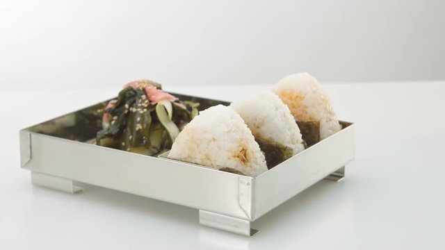 bento with sea kale salad with sesame seeeds and three onigiri rice balls on white studio space. Pure japanese food