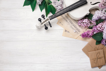 A bouquet of lilacs with violin, letter and music sheet on a white wooden table. Top wiev with...