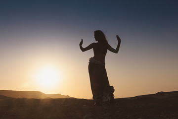Woman dancing to the famous Arab belly dance. With sunset in the arid desert plain of Namibe. Africa. Angola.