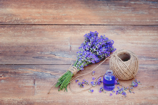 Fresh bouquet of lavender, hemp ball and lavender essential oil on brown wooden background.