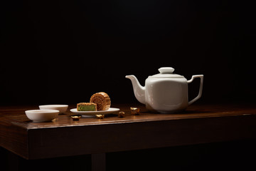 traditional chinese mooncakes, tea pot and gold ingots on wooden table isolated on black with copy space