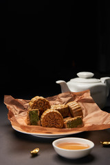 selective focus of traditional chinese mooncakes, tea pot and gold ingots on wooden table isolated on black