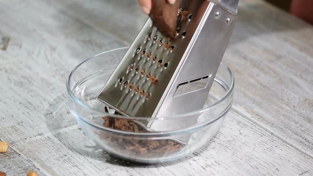 Woman grates chocolate dough in the glass bowl.