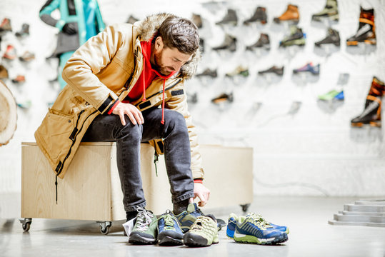 Man in winter jacket trying shoes for mountain hiking sitting in the fitting room of the modern sports shop