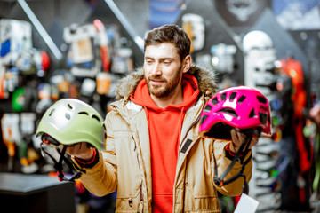 Fototapeta na wymiar Man in winter jacket choosing mountaineer equipment holding helmets for hiking in the sports shop