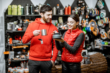 Young couple dressed in red sportswear choosing dishes for camping in the shop with travel equipment