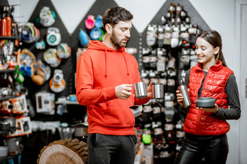 Fototapeta na wymiar Young couple dressed in red sportswear choosing dishes for camping in the shop with travel equipment