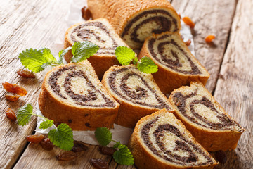 Rustic style poppy roll with raisins, nuts decorated with mint close-up on parchment on a wooden table. horizontal