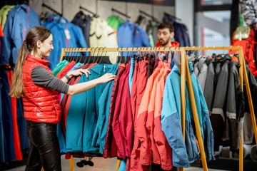 Young woman choosing winter clothes picking up down jackets on the hanger in the sports shop