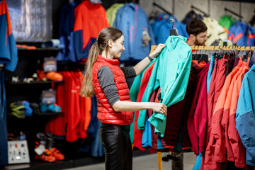 Fototapeta na wymiar Young woman choosing winter clothes picking up down jackets on the hanger in the sports shop