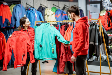 Young woman choosing between red and turquoise jacket standing with boyfriend in the sports shop © rh2010