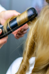 Naklejka premium Close-up photo professional hairdresser uses flat iron for making curls on beautiful blonde hair